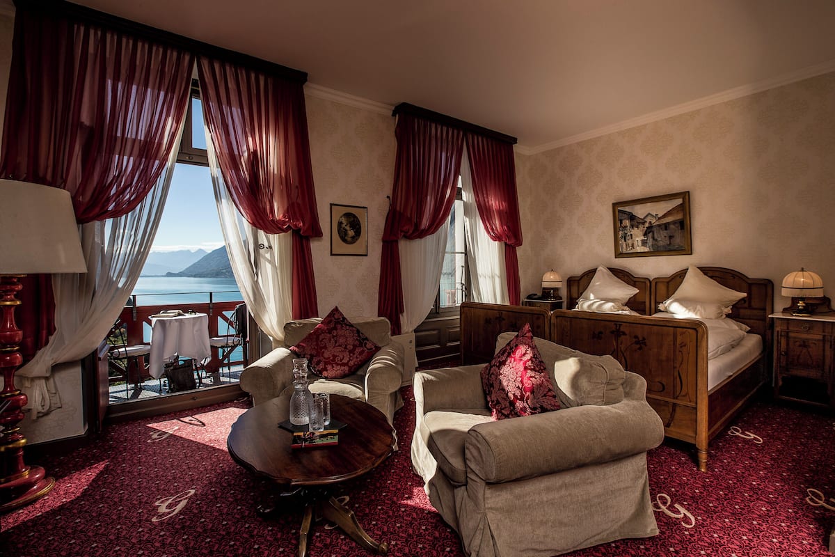 Um quarto com uma cama, duas poltronas, uma mesa pequena e vista para o mar.