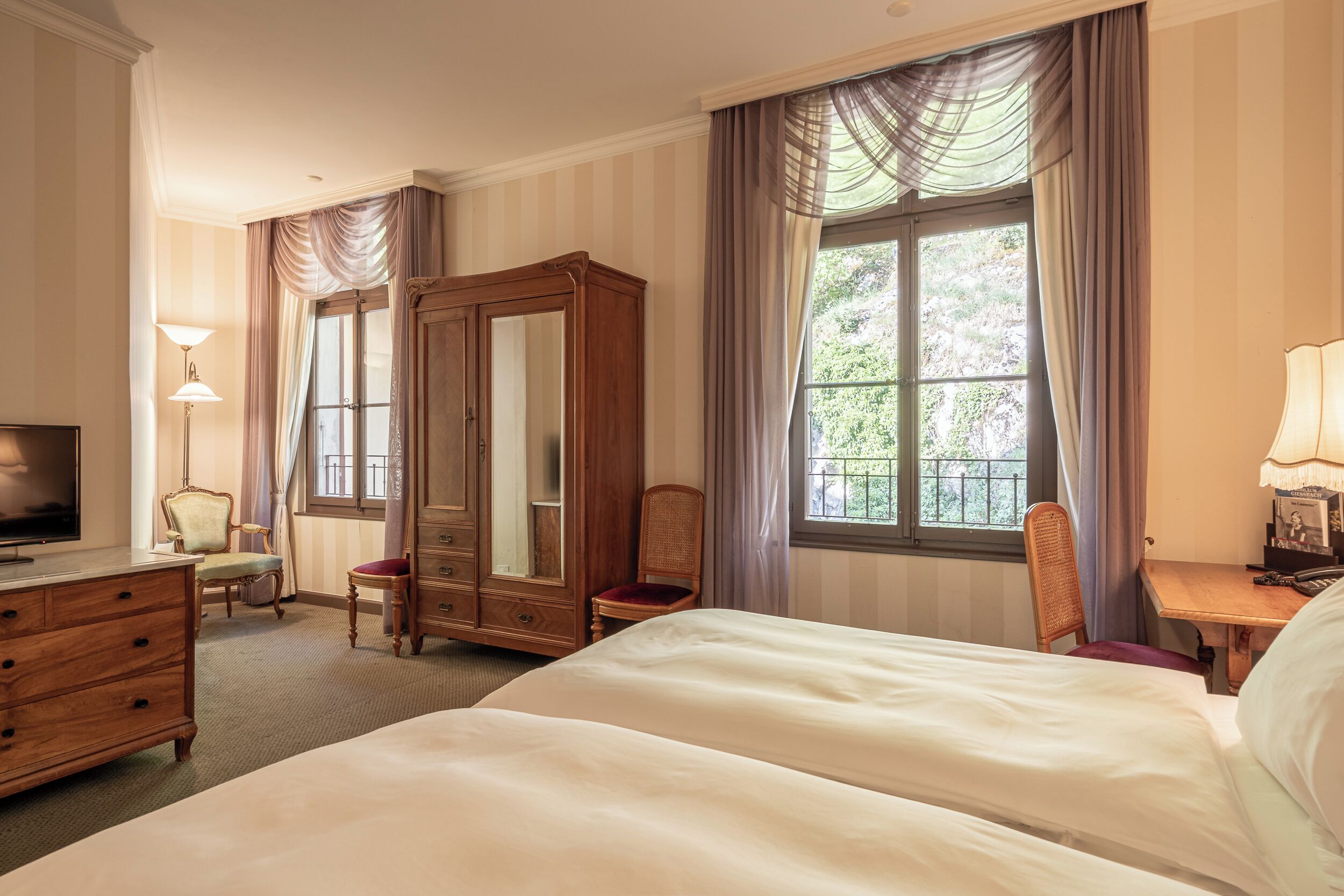 Habitación de hotel con una cama grande, un armario, un escritorio con lámpara, una silla y un televisor.