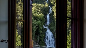 Une vue sur une cascade à plusieurs niveaux, aperçue à travers une fenêtre ouverte, et entourée d’une forêt dense.