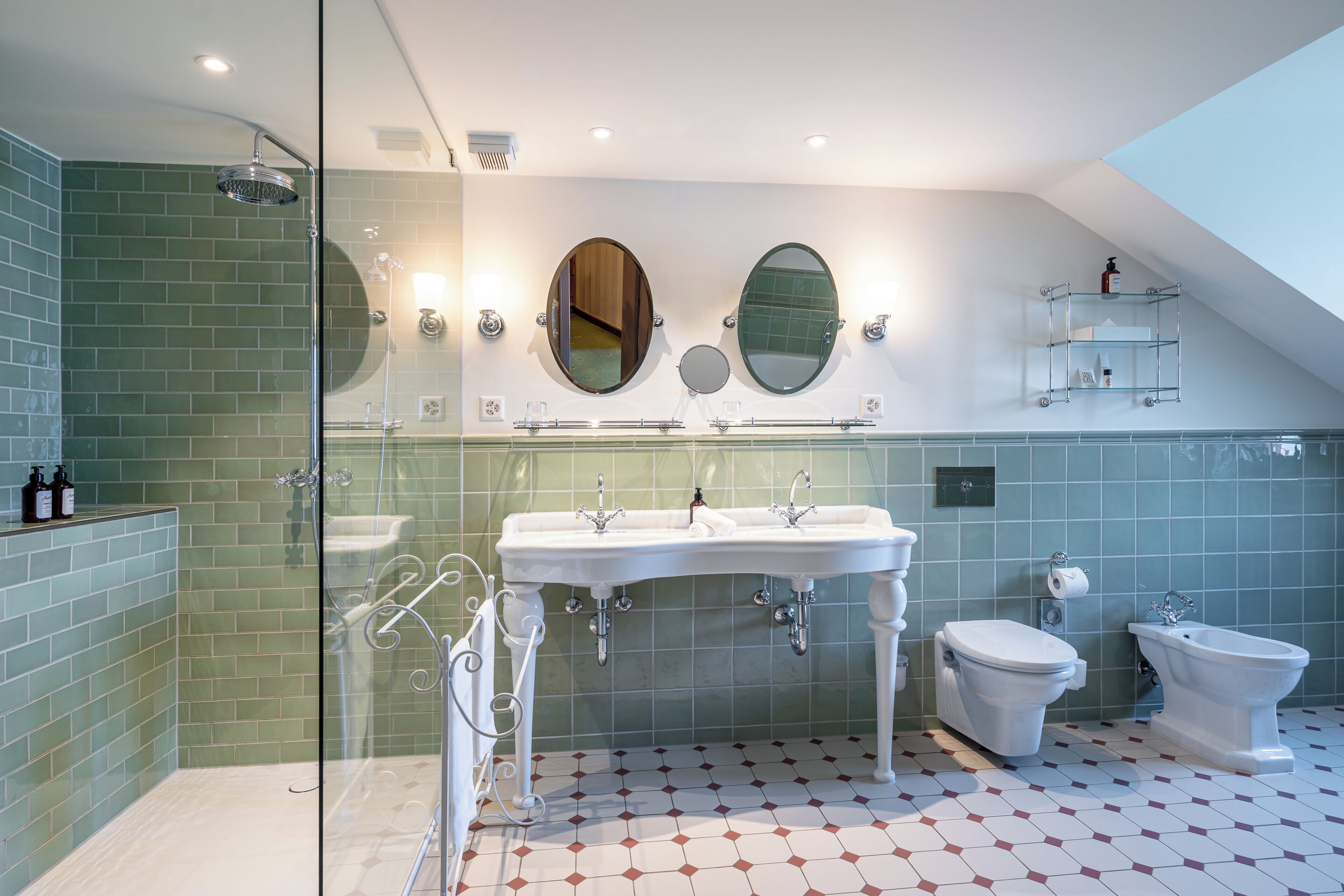 Une salle de bain moderne dotée d’une douche à parois de verre, de deux lavabos, de toilettes et d’un bidet.