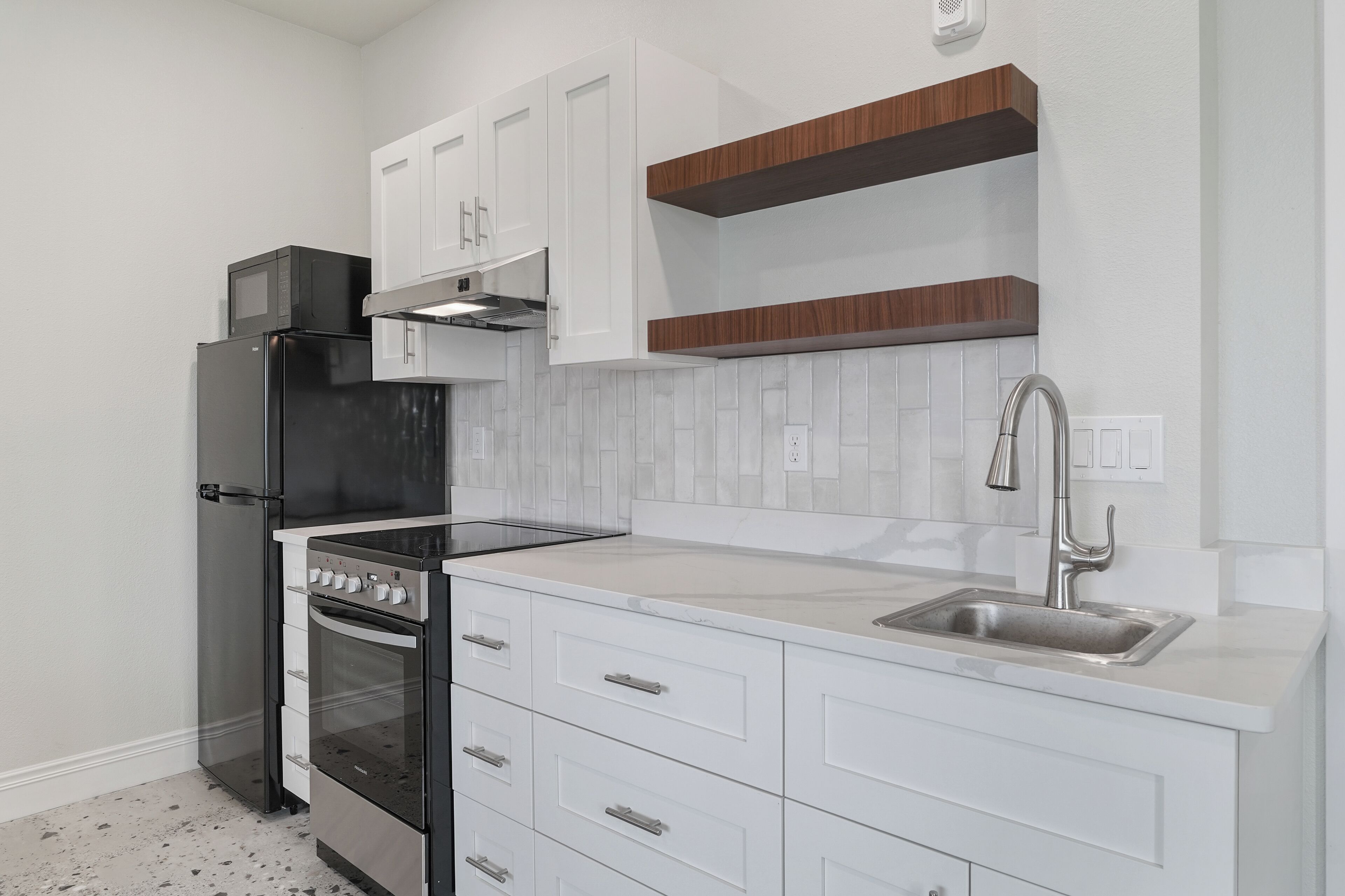 A modern kitchen with white cabinetry, a black refrigerator, a stainless steel stove, and a wooden countertop.