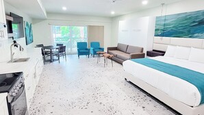 Un soggiorno moderno con un divano bianco, un'area pranzo con sedie blu e una cucina con mobili bianchi.