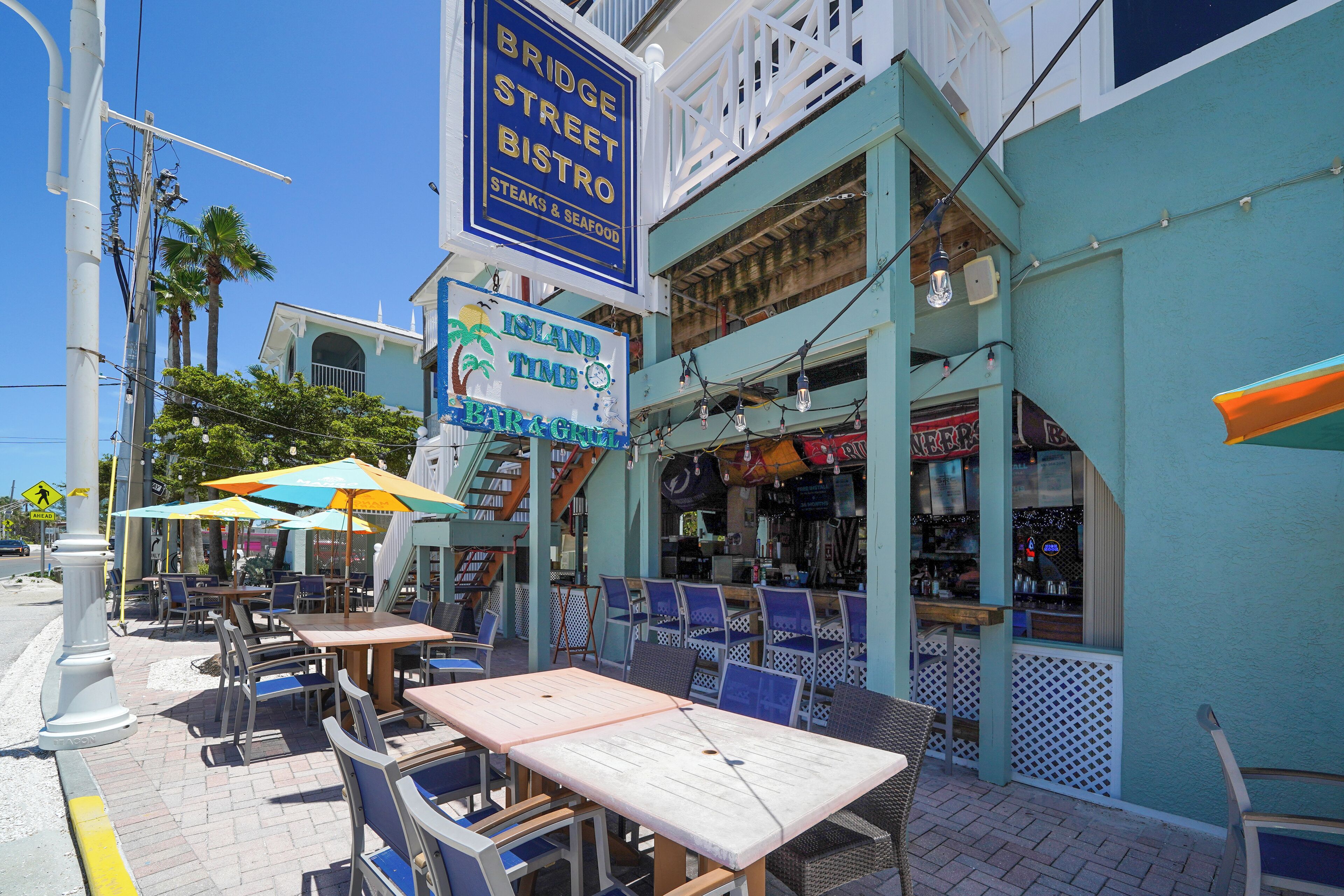 An outdoor dining area with tables and chairs, a bar, and a sign for 'Island Times Bar & Grill'.
