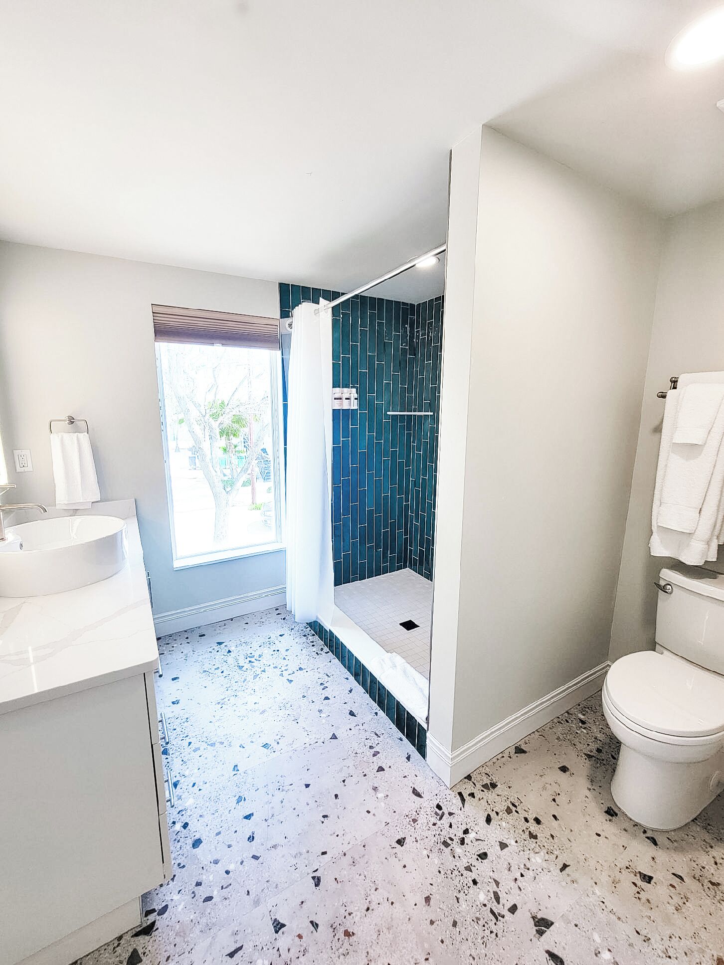A modern bathroom with a white sink, a shower with a blue tiled wall, and a toilet.