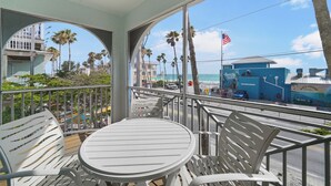Un balcone con tavolo e sedie, vista su una spiaggia con palme e un edificio blu con una bandiera americana.