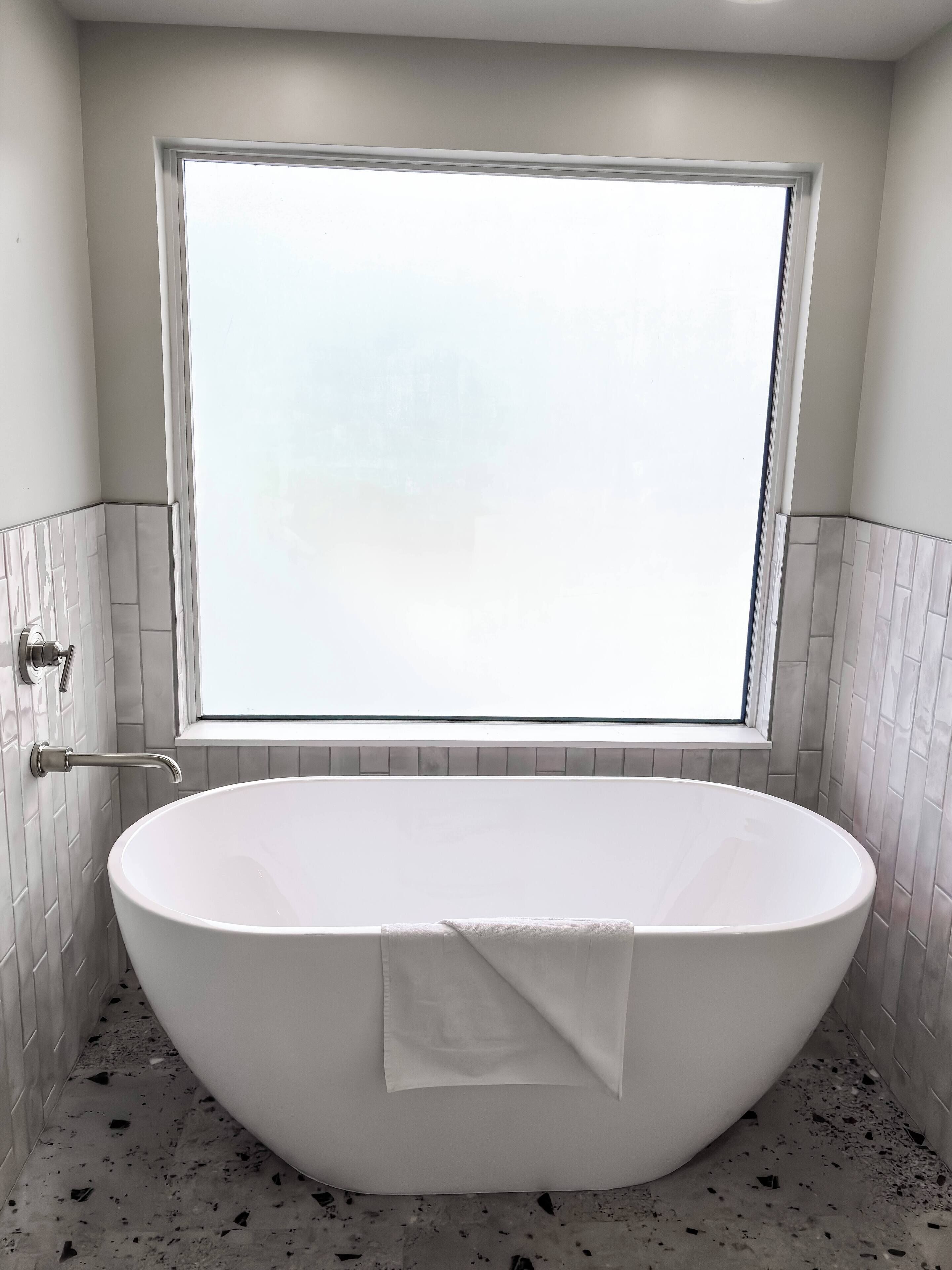 Ein modernes Badezimmer mit einer freistehenden Badewanne, einem Fenster darüber und gefliesten Wänden.