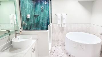 A modern bathroom with a freestanding bathtub, a large mirror, and a shower with a green mosaic wall.