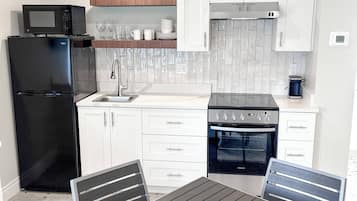 Una cocina moderna con armarios blancos, un refrigerador negro, un microondas, una estufa y un fregadero. Hay una mesa de comedor con dos sillas.