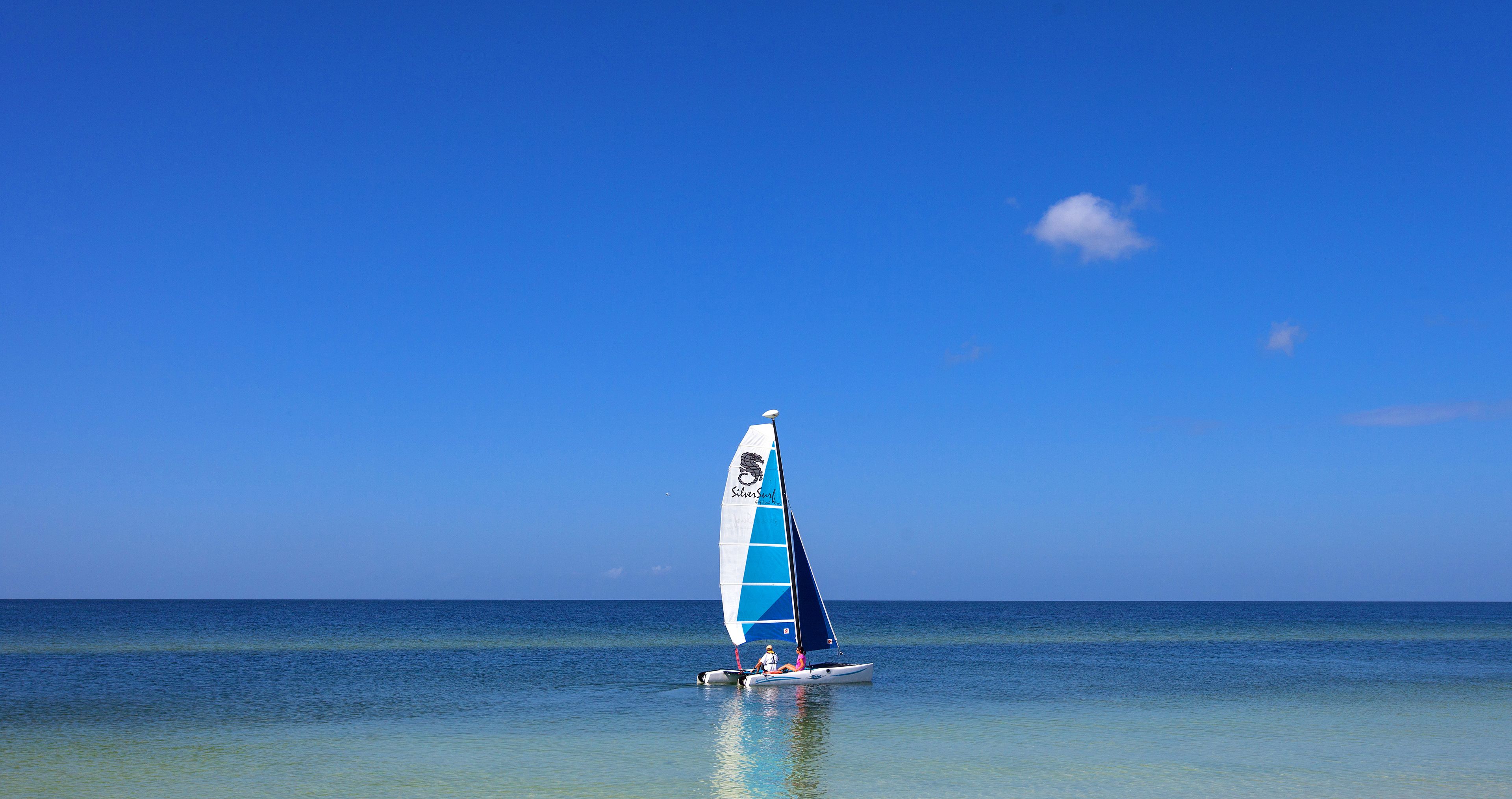 A sailboat with a blue sail on calm, clear water.