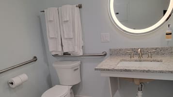 Un baño moderno con inodoro, lavamanos con encimera de granito, espejo con luz y toallero con toallas.