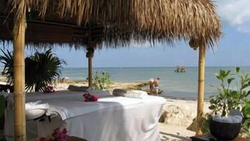 Relax in a beachside retreat with a thatched-roof structure offering shade, a comfortable bed, and a charming table setting.