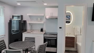 A modern kitchen with white cabinets, a black refrigerator, a microwave, and a stove. There is a dining area with a round table and chairs.