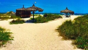 A beach path leading to thatched-roof huts with a clear blue sky. - Silver Surf Gulf Beach Resort (Bradenton Beach)