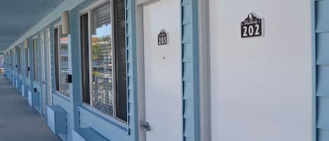Una hilera de habitaciones de motel con puertas numeradas, un corredor cubierto y vista a la calle.