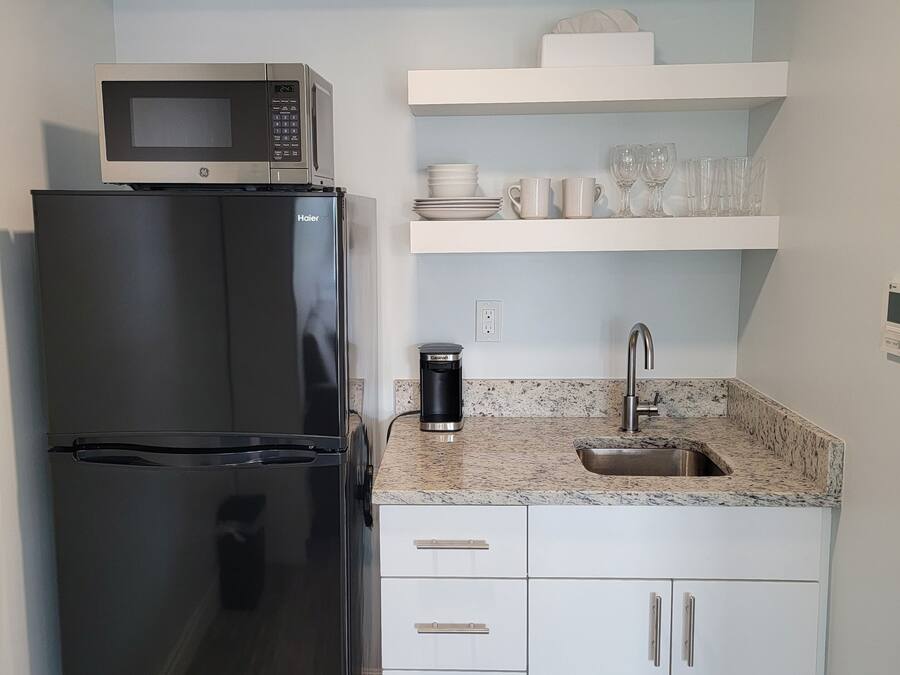 A compact kitchen with a black refrigerator, a microwave, a coffee maker, and a granite countertop.
