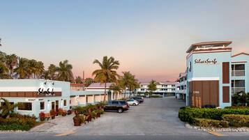 A hotel with a sign reading "SilverSurfs Golf & Beach Resort," featuring a parking area, palm trees, and a clear sky.