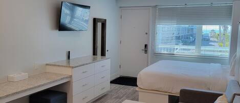 A modern bedroom with a bed, a TV, a desk, and a window with blinds.