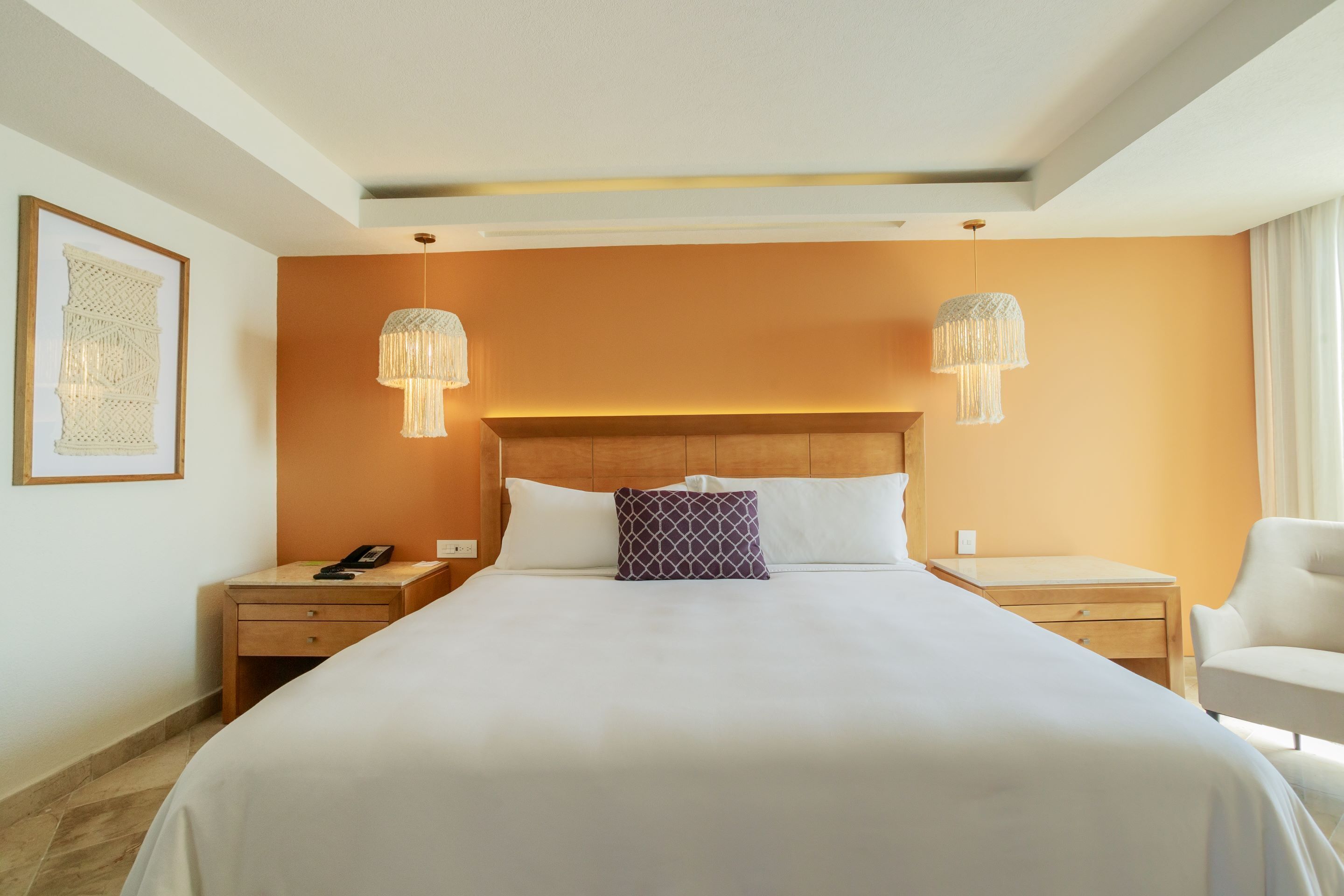 Habitación de hotel con una cama grande, dos mesitas de noche, una silla y un cuadro enmarcado en la pared.