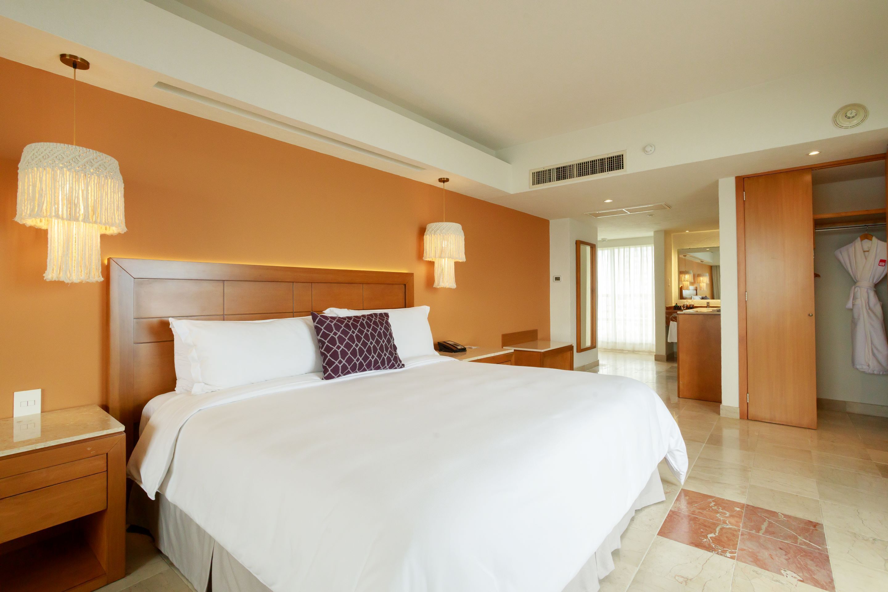 Une chambre d’hôtel avec un grand lit, des tables de chevet, une armoire et une salle de bain visible à travers une porte ouverte.