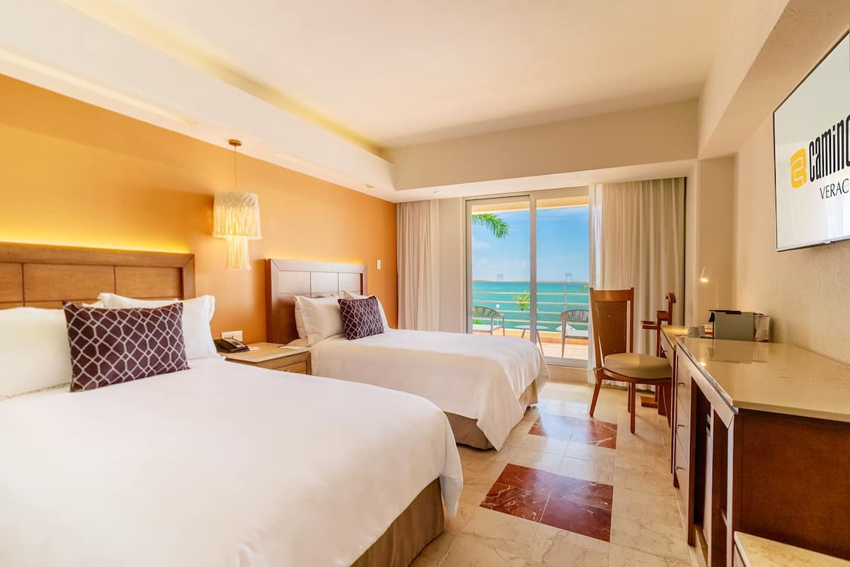A hotel room with two beds, a desk, and a view of the ocean.