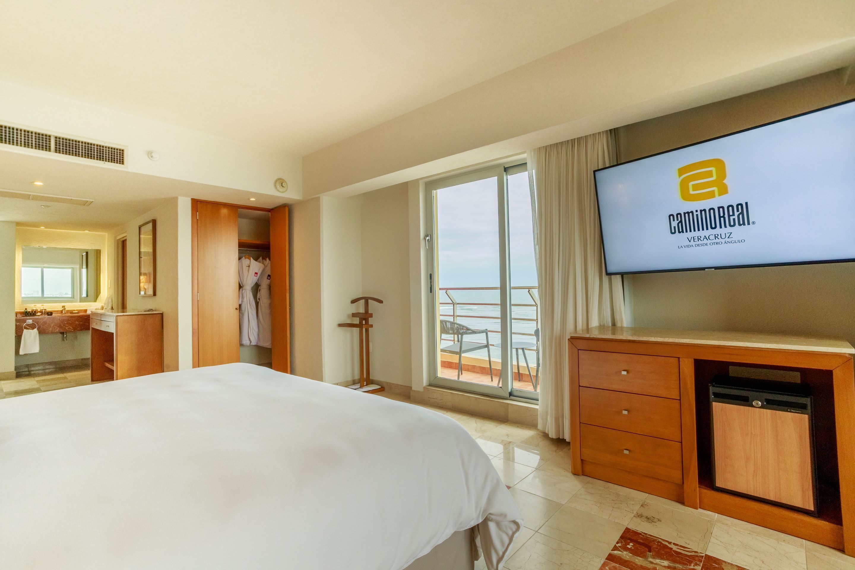 Habitación de hotel con una cama grande, un televisor montado en la pared, un escritorio de madera y un balcón con vistas.