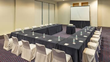 Une salle de conférence avec une longue table, des chaises, un écran de projection et des bouteilles d’eau posées sur la table.