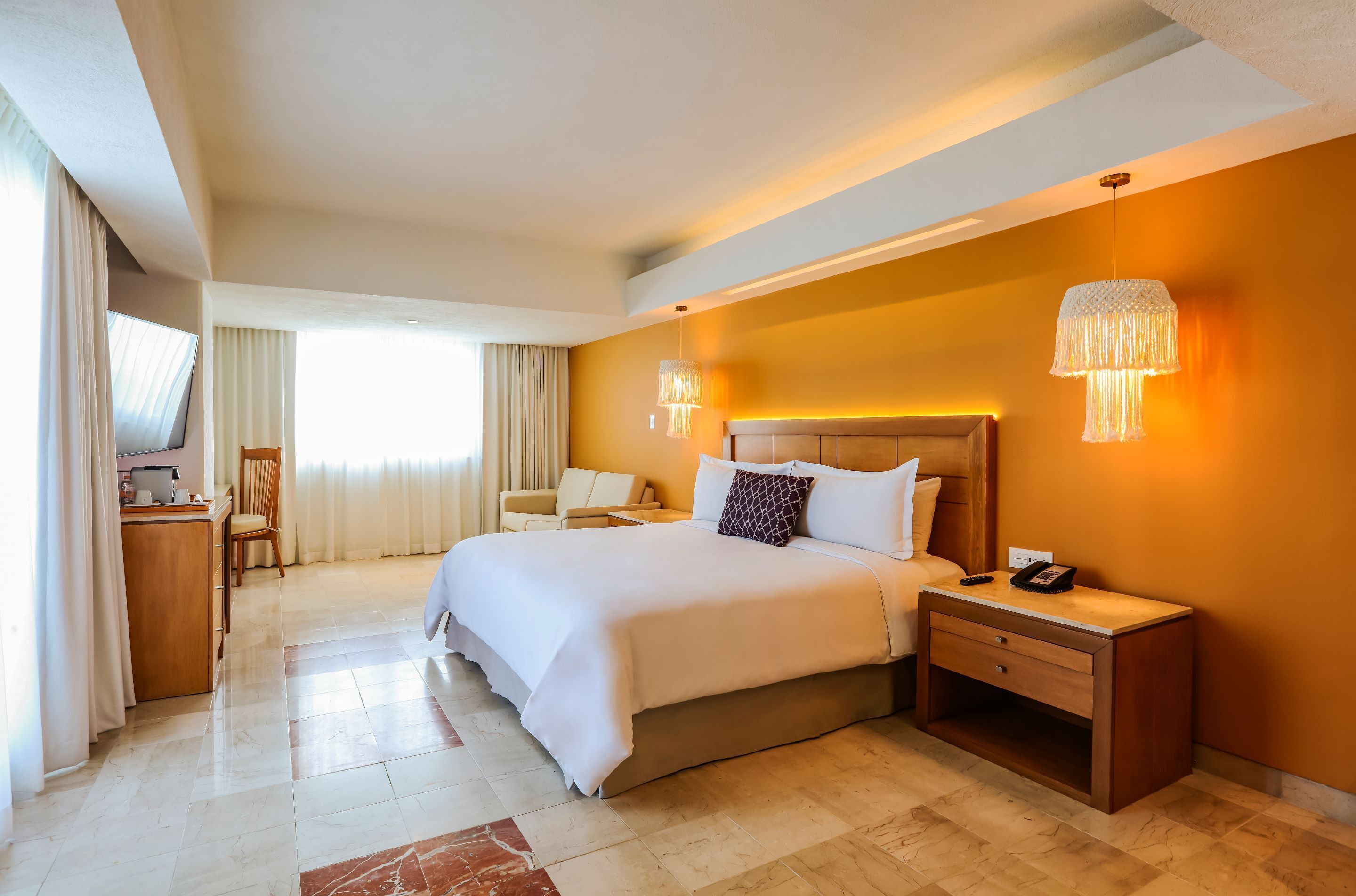 A hotel room with a large bed, bedside tables, a desk, and a TV.