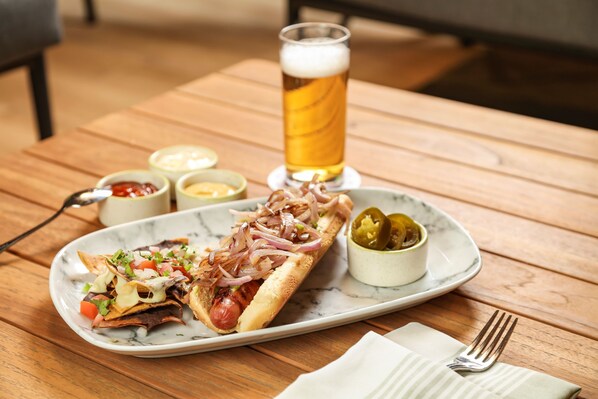A meal with nachos, a hot dog, and a glass of beer on a wooden table. - Camino Real Veracruz (Boca del Río)