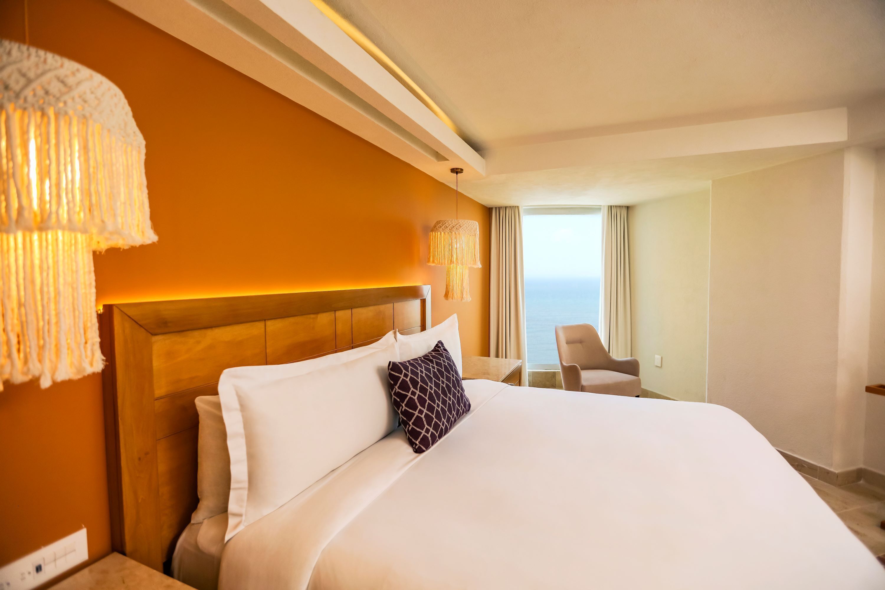 A hotel room with a large bed, a wooden headboard, a view of the sea, and a seating area with a table and chairs.
