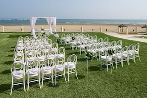 Ein Strandhochzeitsaufbau mit weißen Stühlen und einem Baldachin.