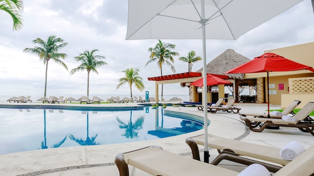A poolside area with lounge chairs and umbrellas, palm trees, and a view of the ocean. - Camino Real Veracruz (Boca del Río)