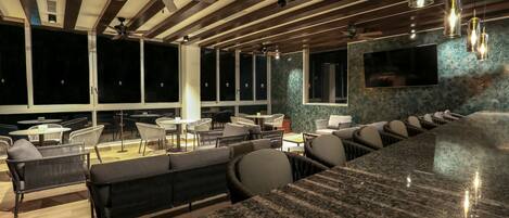 Uma área de bar moderna com bancada de granito, assentos com almofadas, ventiladores de teto e iluminação pendente.