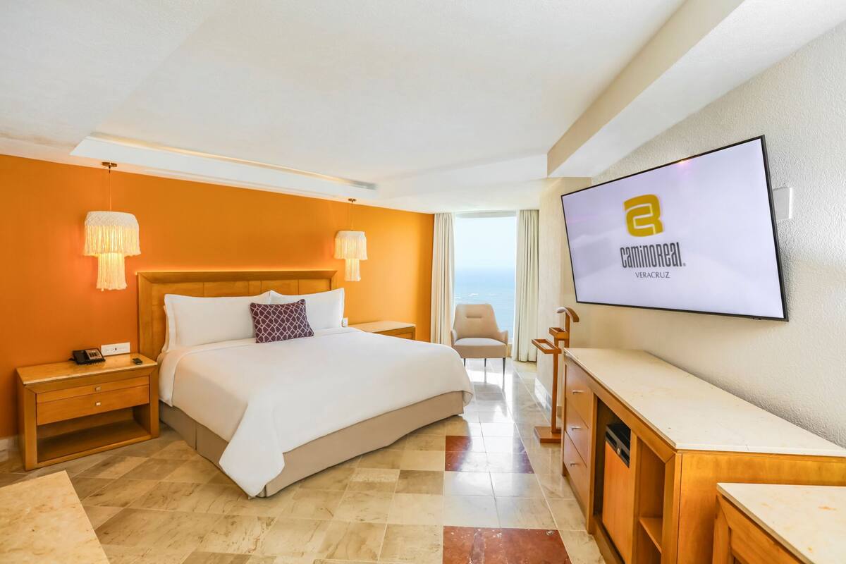 A hotel room with a large bed, a TV mounted on the wall, and a view of the sea.