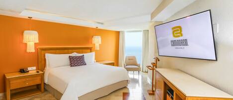 A hotel room with a large bed, a TV mounted on the wall, and a view of the sea.