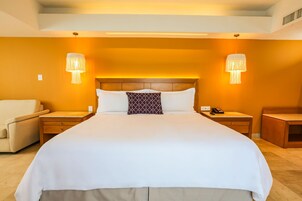 Una habitación de hotel con una cama grande, dos mesitas de noche, una silla y dos lámparas de pared.
