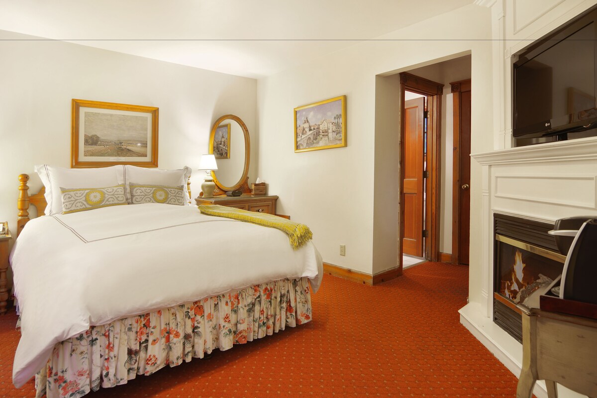 A hotel room with a large bed, a fireplace, a wooden door, and a framed picture on the wall.