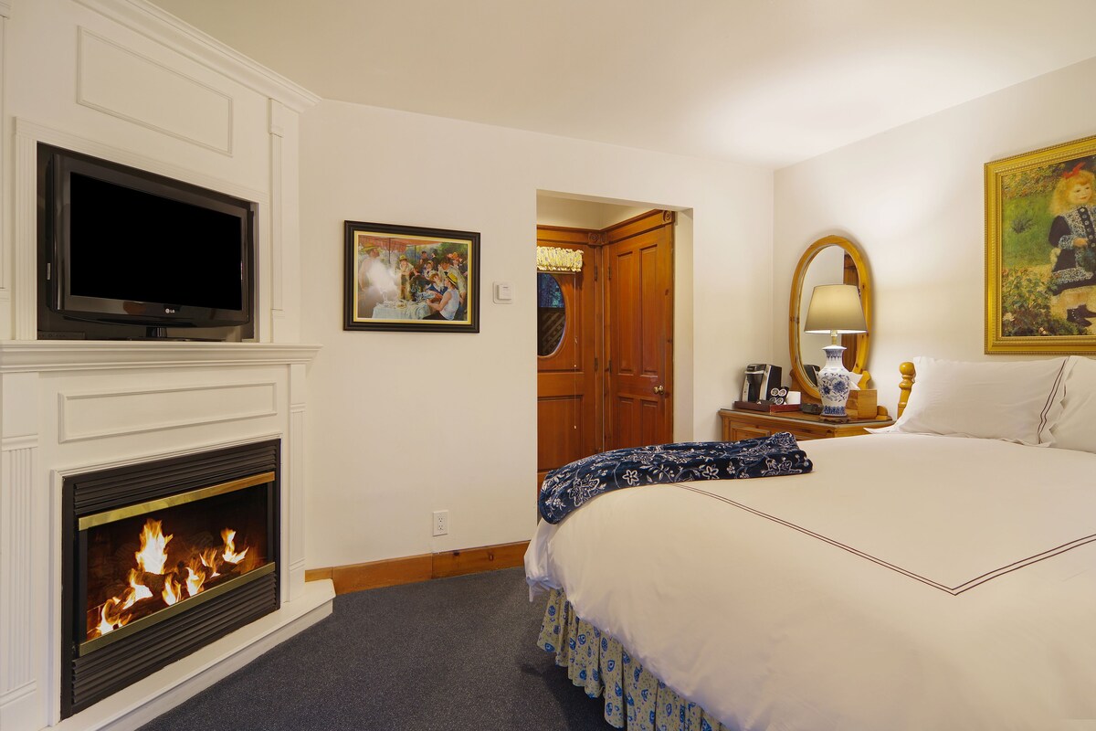 A hotel room with a fireplace, a bed, a television, and a painting.