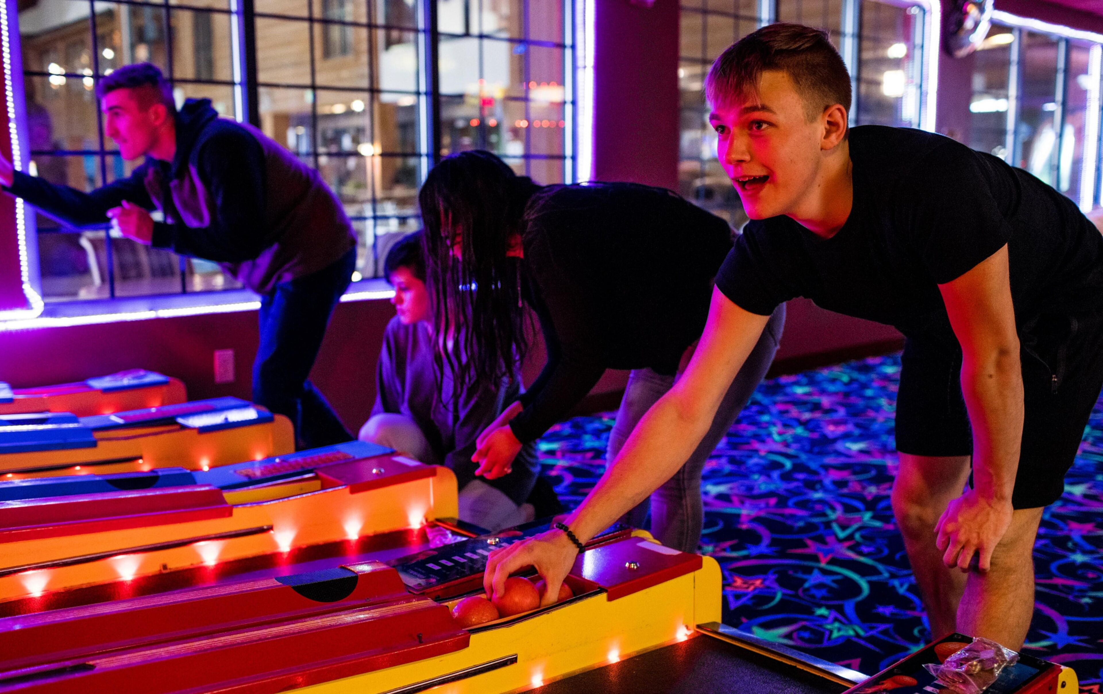 Een groep mensen speelt een spel op een tafel met verlichte borden, in een kamer met grote ramen en een kamerbreed tapijt.
