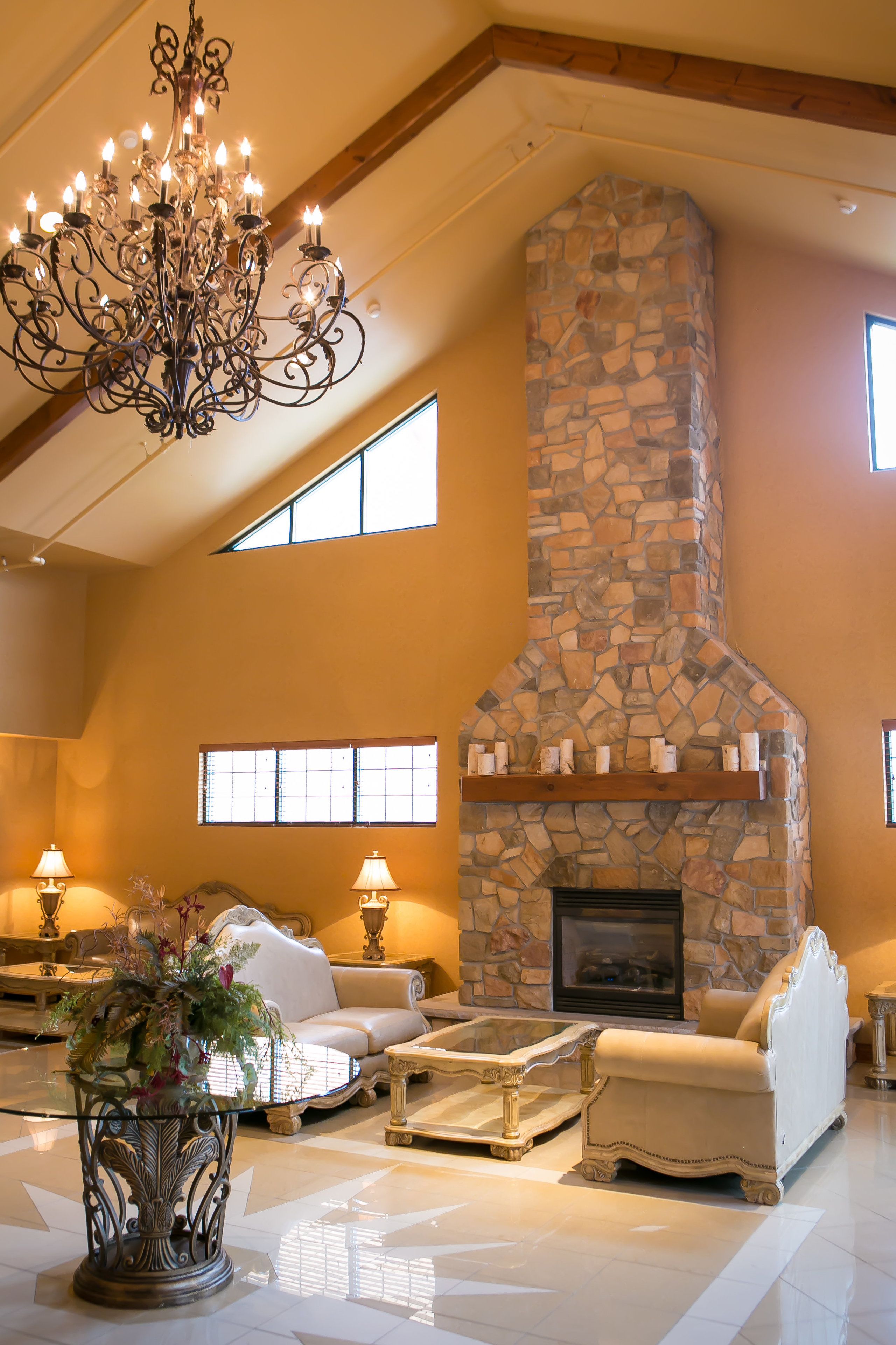 A spacious living room with a stone fireplace, elegant furniture, and a chandelier.
