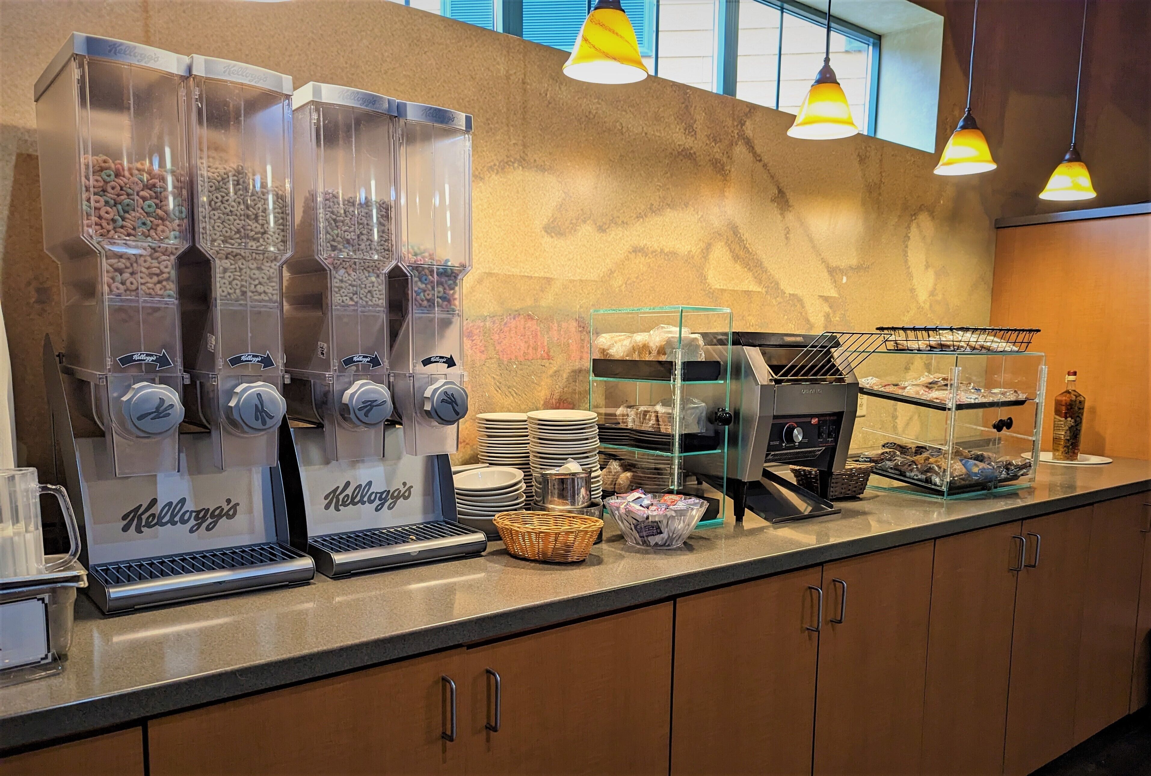 A breakfast bar with multiple Kellogg's cereal dispensers, a coffee machine, and a variety of breakfast items.