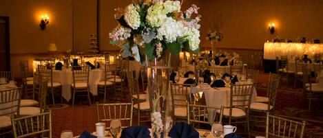 Un salón de banquetes con mesas redondas dispuestas para un evento formal, con candelabros, centros de mesa florales y vajilla ordenada.