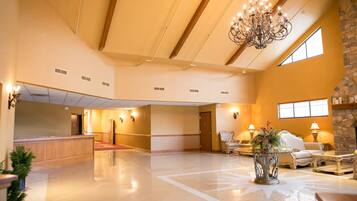 A spacious lobby with a high ceiling, a chandelier, a reception desk, and a seating area with a fireplace.