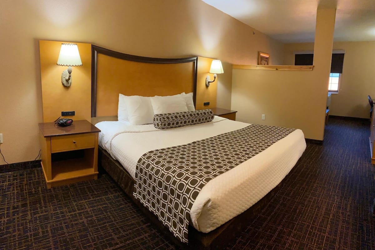 A hotel room with a large bed, two bedside lamps, a nightstand, and a small desk.
