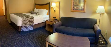A hotel room with a bed, a sofa, a small table, a nightstand, and a lamp.