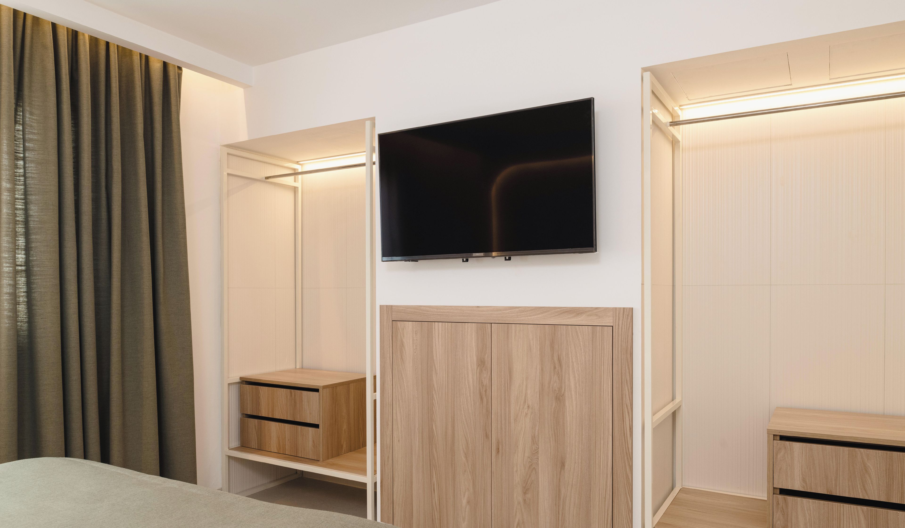 Een moderne slaapkamer met een bed, een garderobe met spiegel en een aan de muur bevestigde televisie.