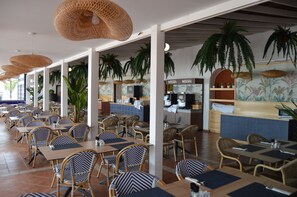 A restaurant with outdoor seating, wicker chairs, and hanging plants.