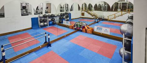 Een sportschool met spiegelwanden, fitnessapparatuur en een vloer van rode en blauwe matten.
