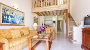 A spacious living room with a high ceiling, a staircase, and a kitchen in the background.