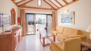 A spacious living area with a wooden ceiling, a sofa, a coffee table, and a television on a wooden cabinet. - Sands Beach Resort (Teguise)