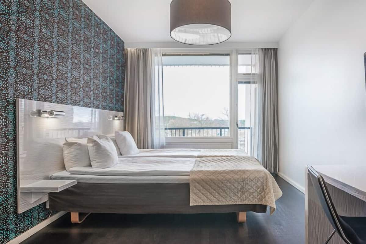 Una habitación de hotel moderna con una cama, un escritorio, un televisor y un ventanal con vistas.
